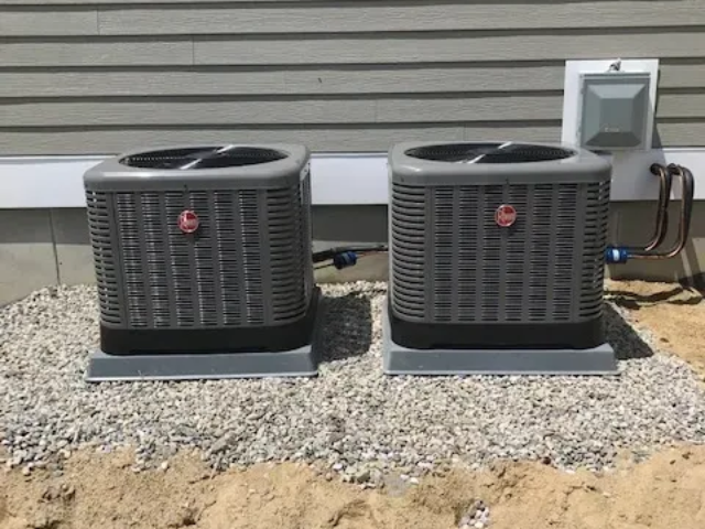 Two outdoor air conditioning units on gravel beside a house wall