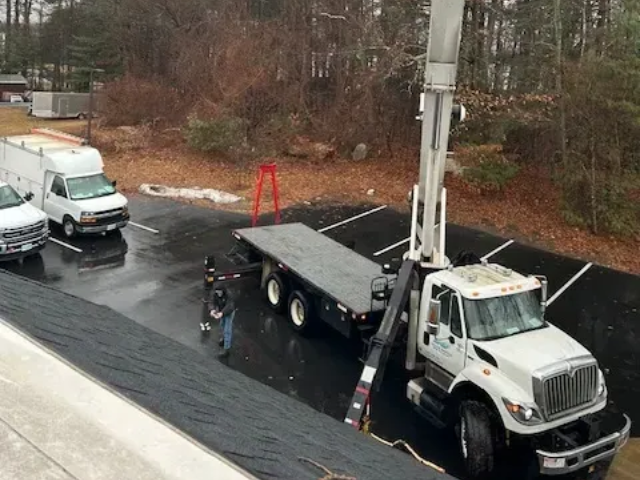 White utility truck with raised boom parked beside a curb on a wet road in a wooded area