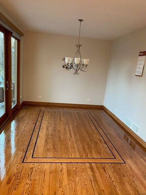 an empty dining room with hardwood floors and a chandelier hanging from the ceiling