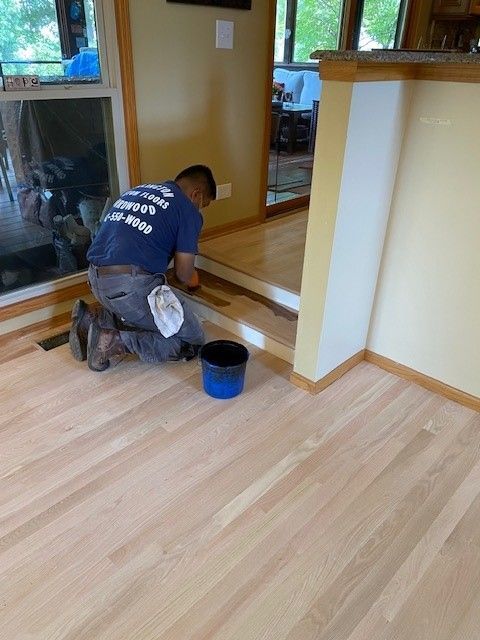 a man wearing a blue shirt that says work on step is kneeling on a wooden floor