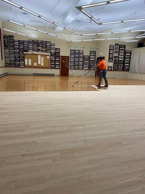 two men are cleaning a wooden floor in a large room