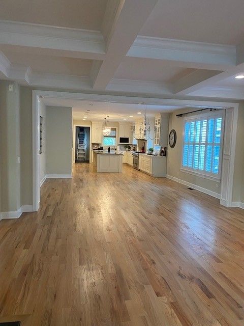 a large empty room with hardwood floors and a kitchen in the background