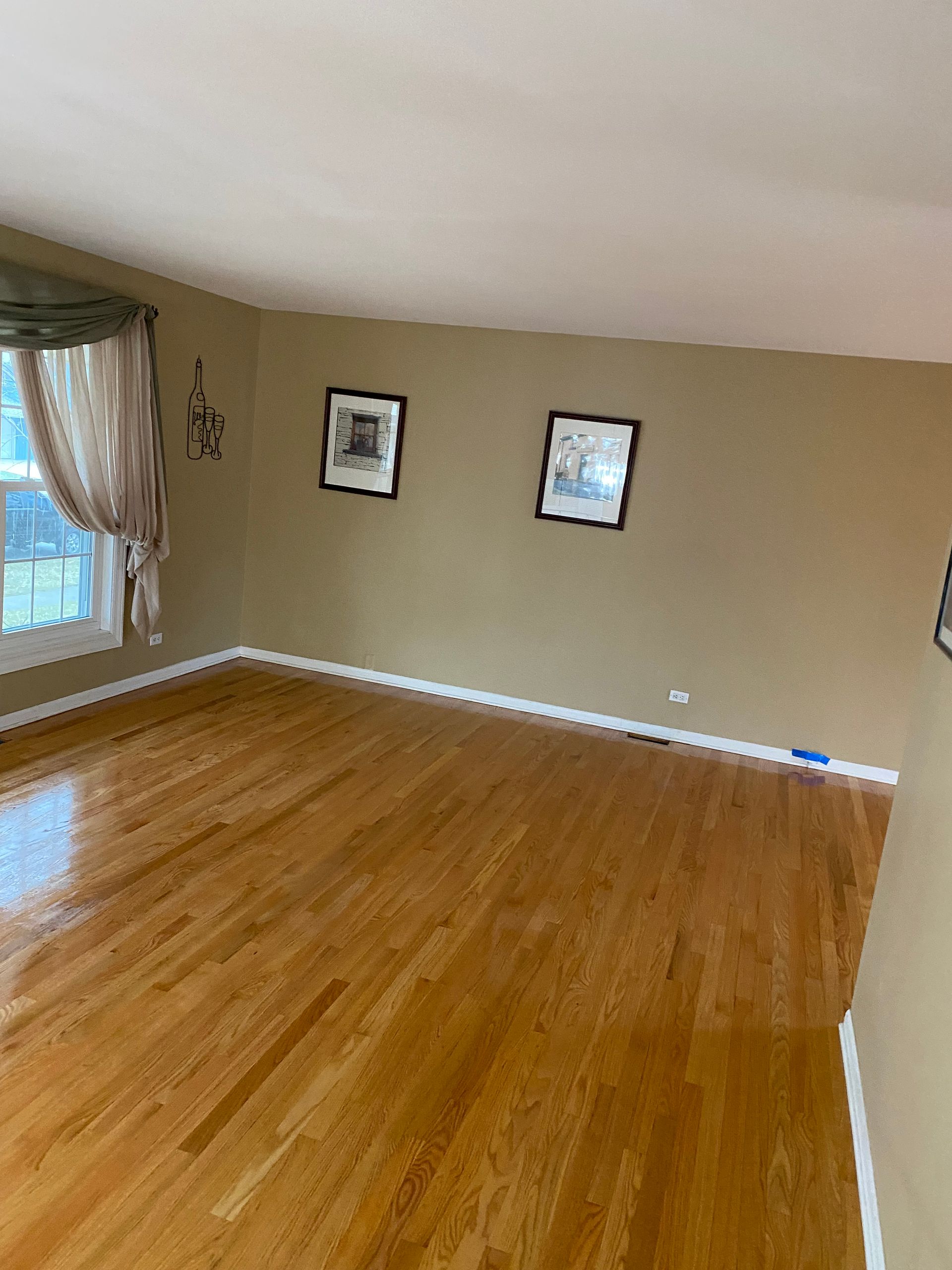 an empty living room with hardwood floors and two pictures on the wall.