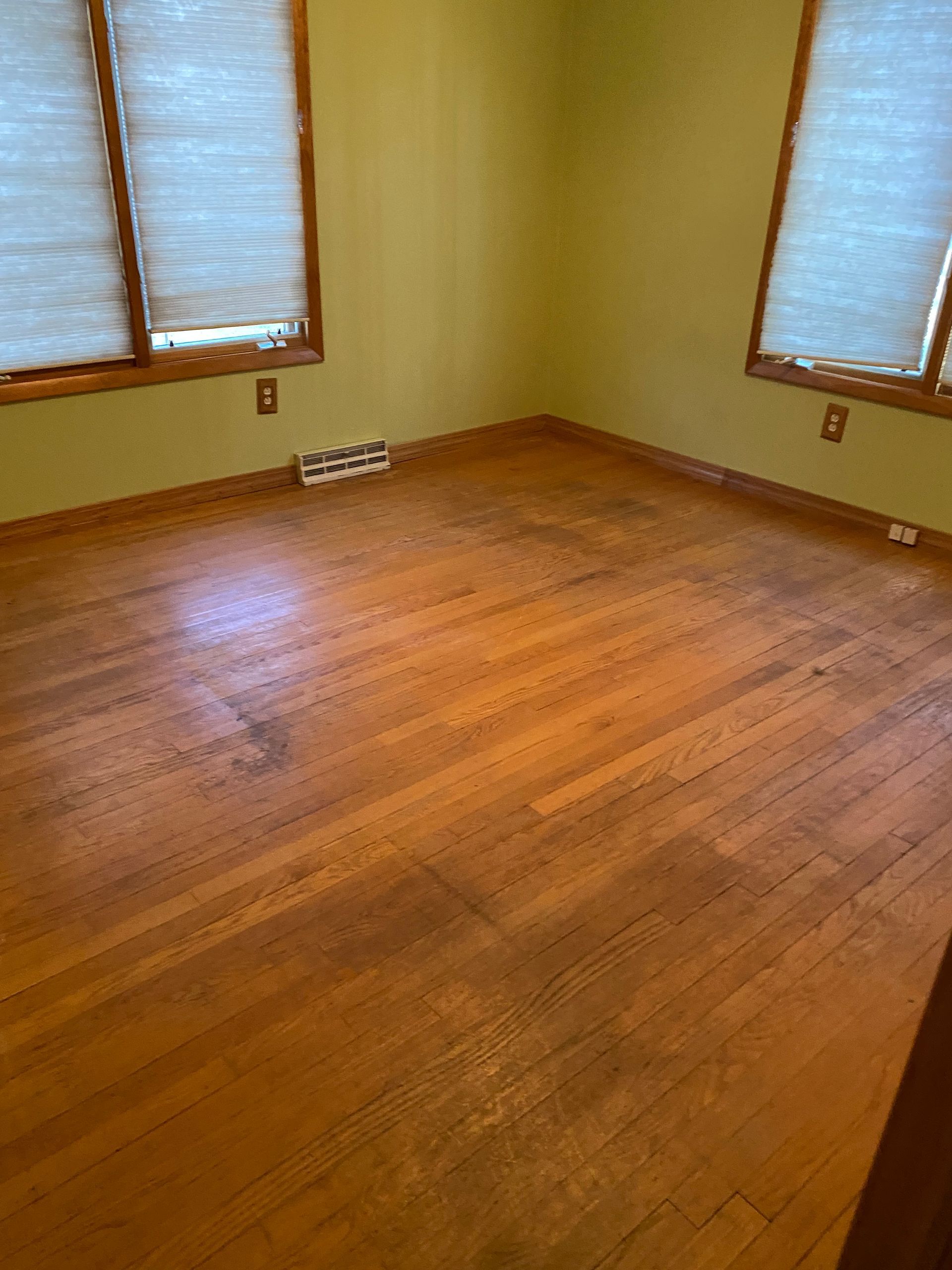 an empty room with hardwood floors and two windows.