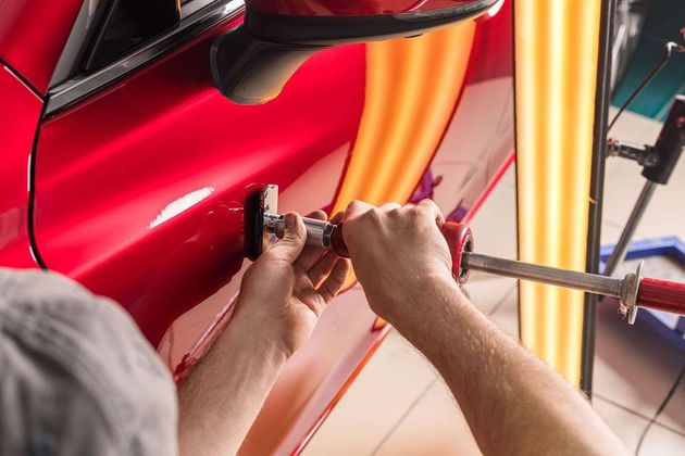 Hands polishing a red car body with a cloth in a workshop