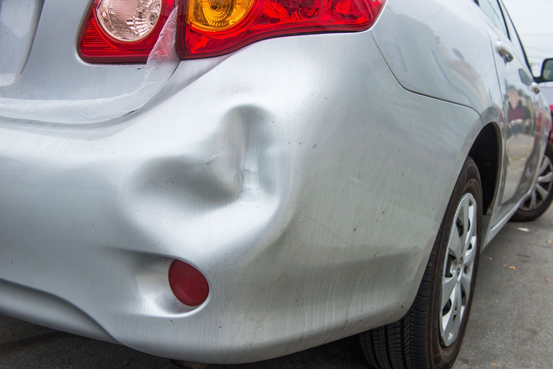 Silver car with a large dent and cracked rear bumper after a collision