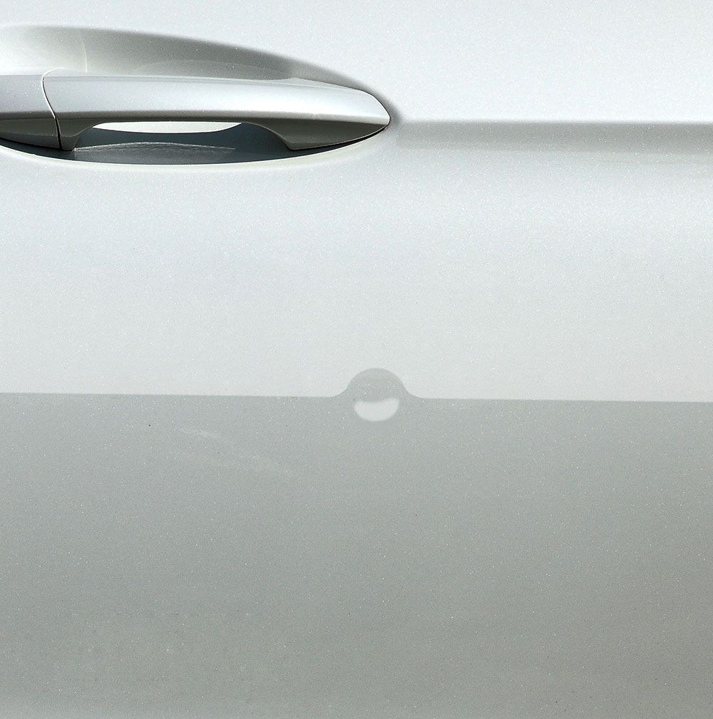 Close-up of a white car door handle with a small circular paint chip below it.