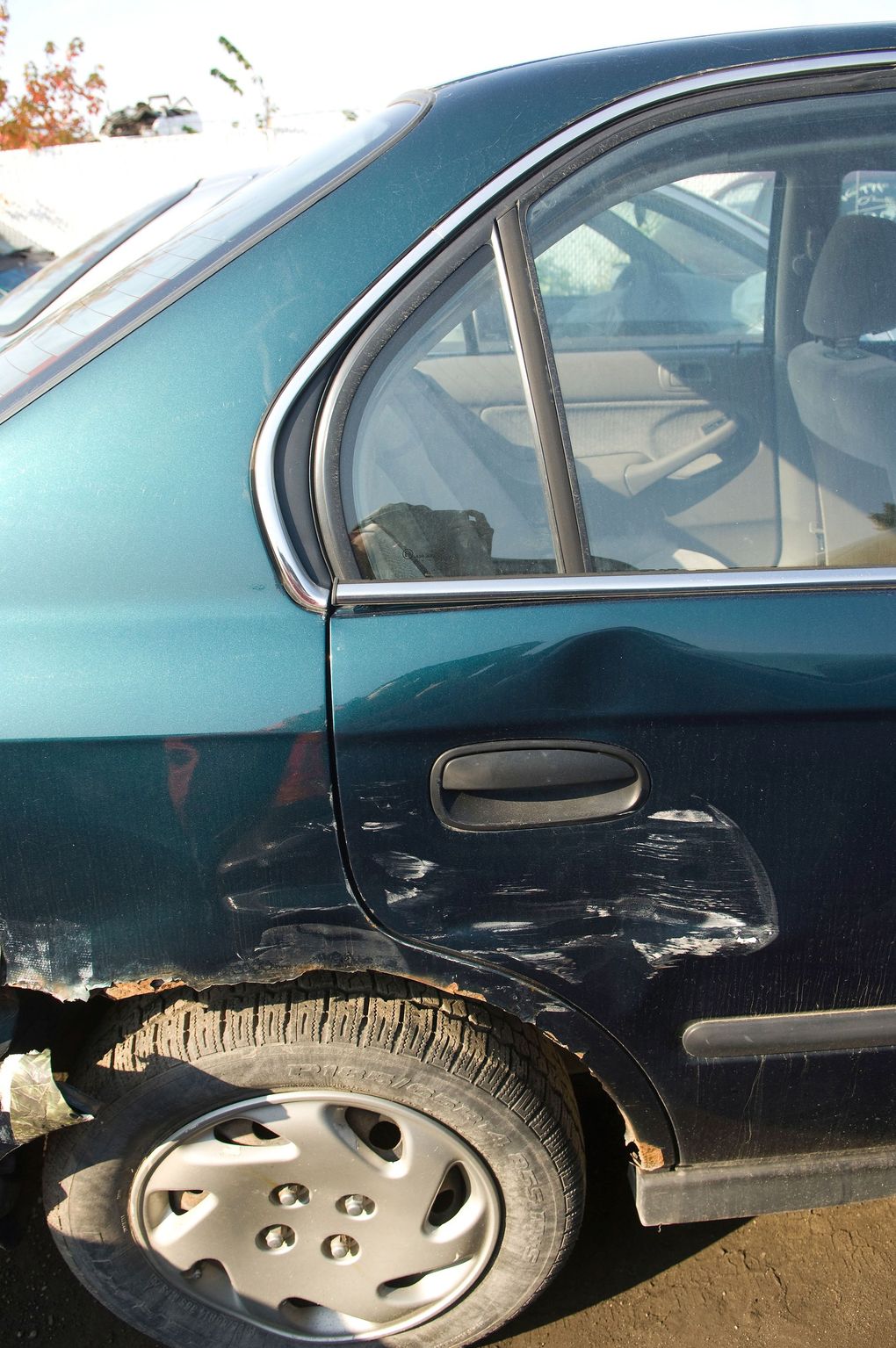 Damaged teal sedan with dented rear door and scratched body panel