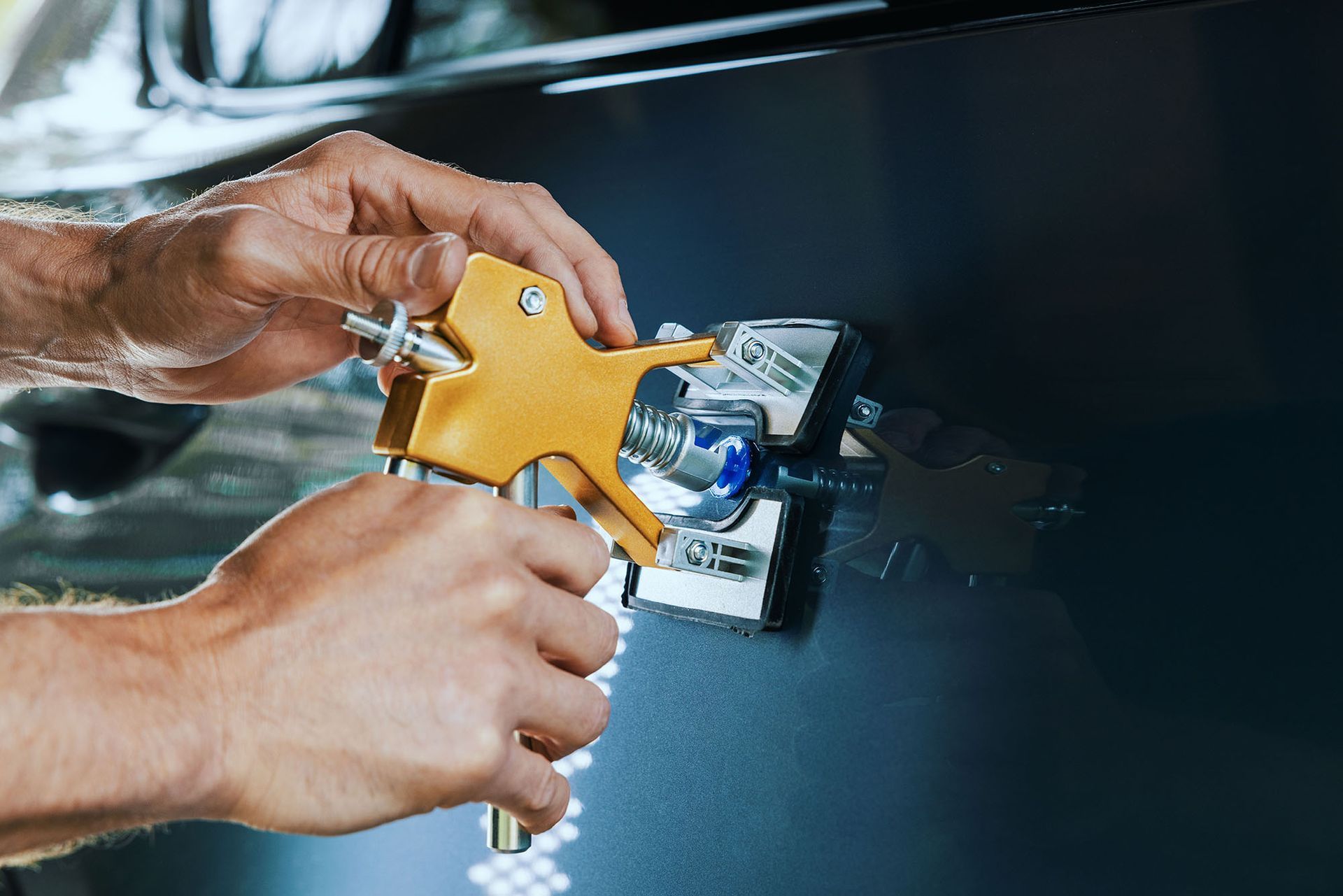 Hands using a yellow spray gun to paint a dark car door