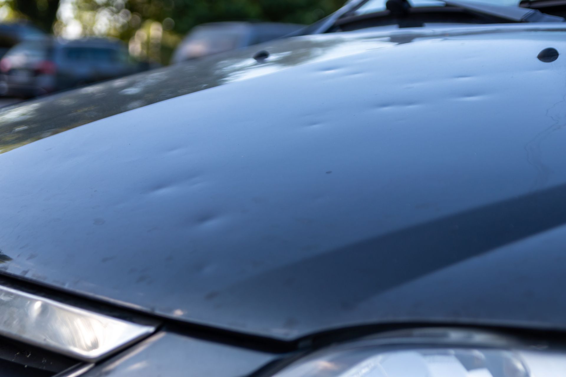 Close-up of a blue car hood with headlights visible outdoors