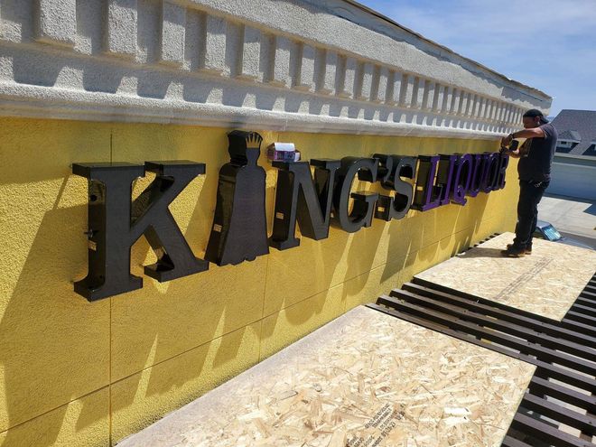 A man is standing next to a yellow sign that says kings liquor.