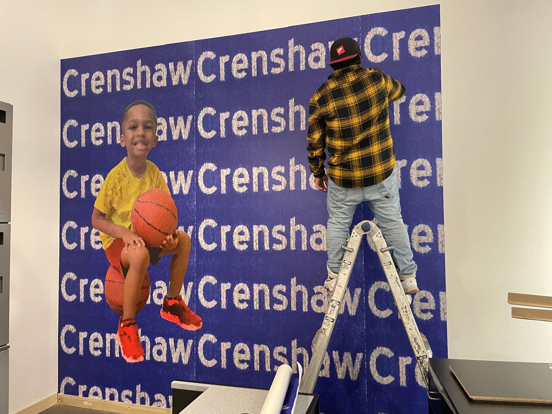 A boy holding a basketball in front of a wall that says crenshaw