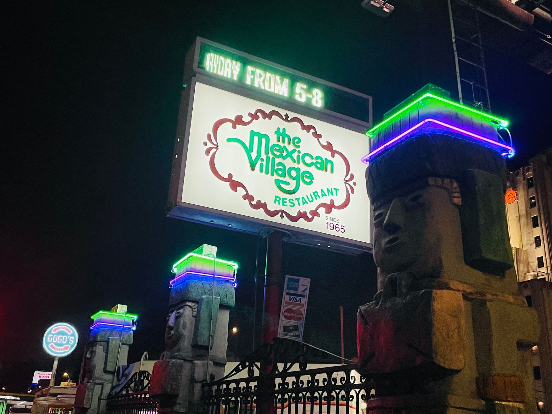 A sign for the mexican village restaurant is lit up at night