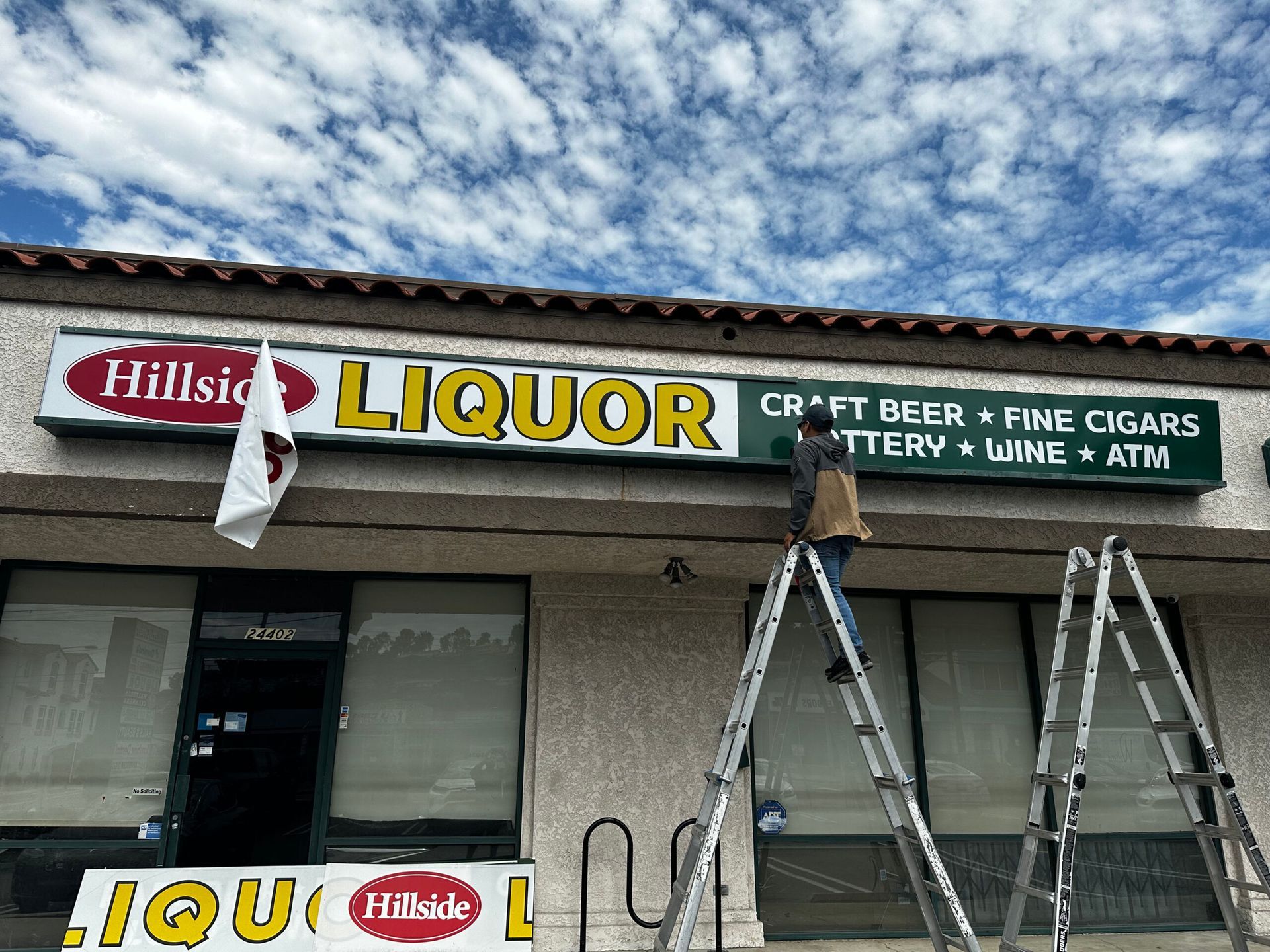 A man is standing on a ladder in front of a liquor store.