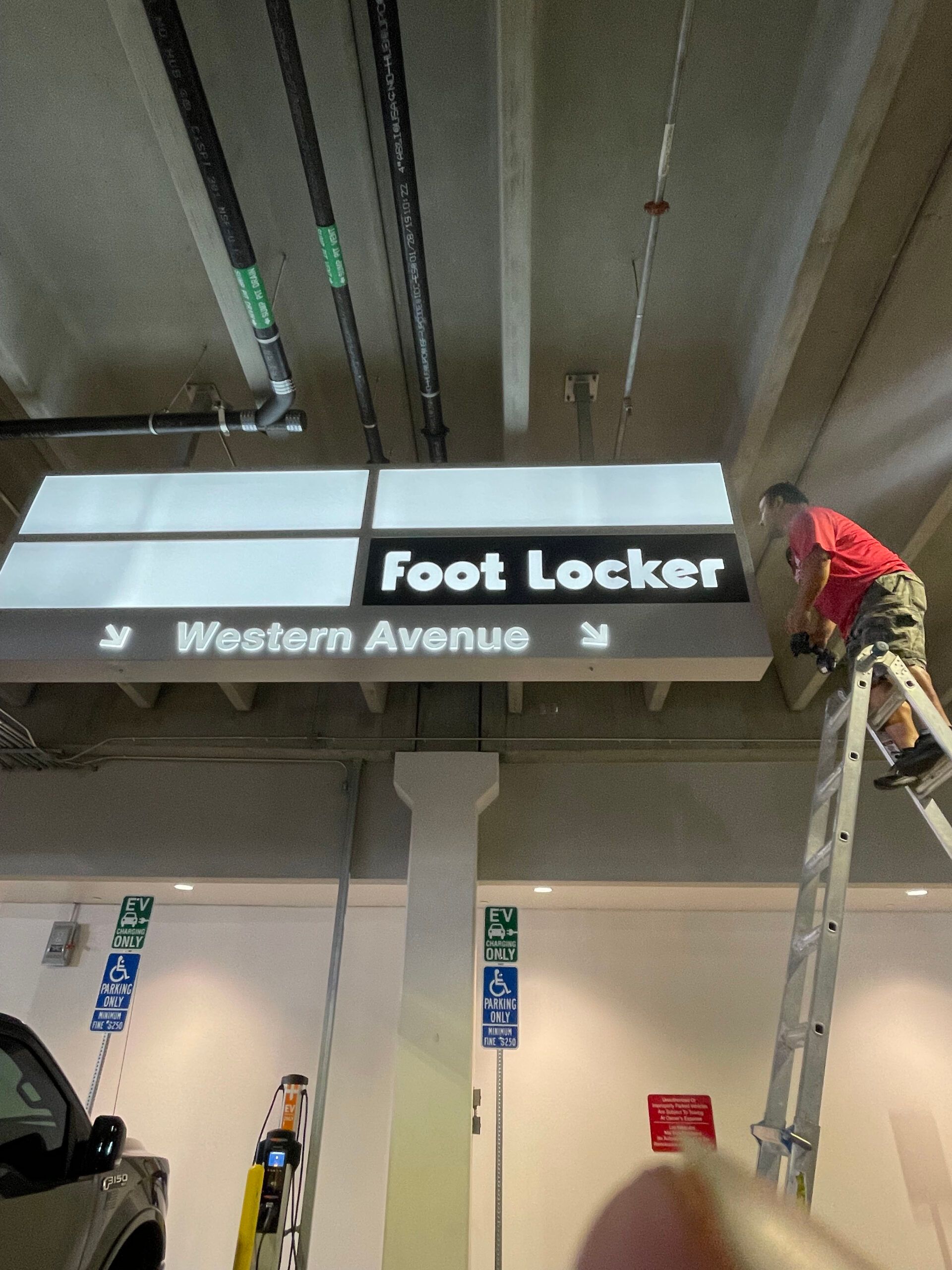 A man on a ladder working on a sign for the foot locker