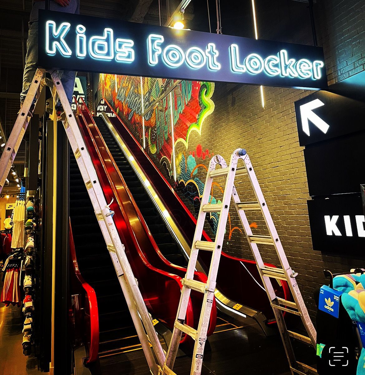 An escalator in a store with a sign that says kids foot locker