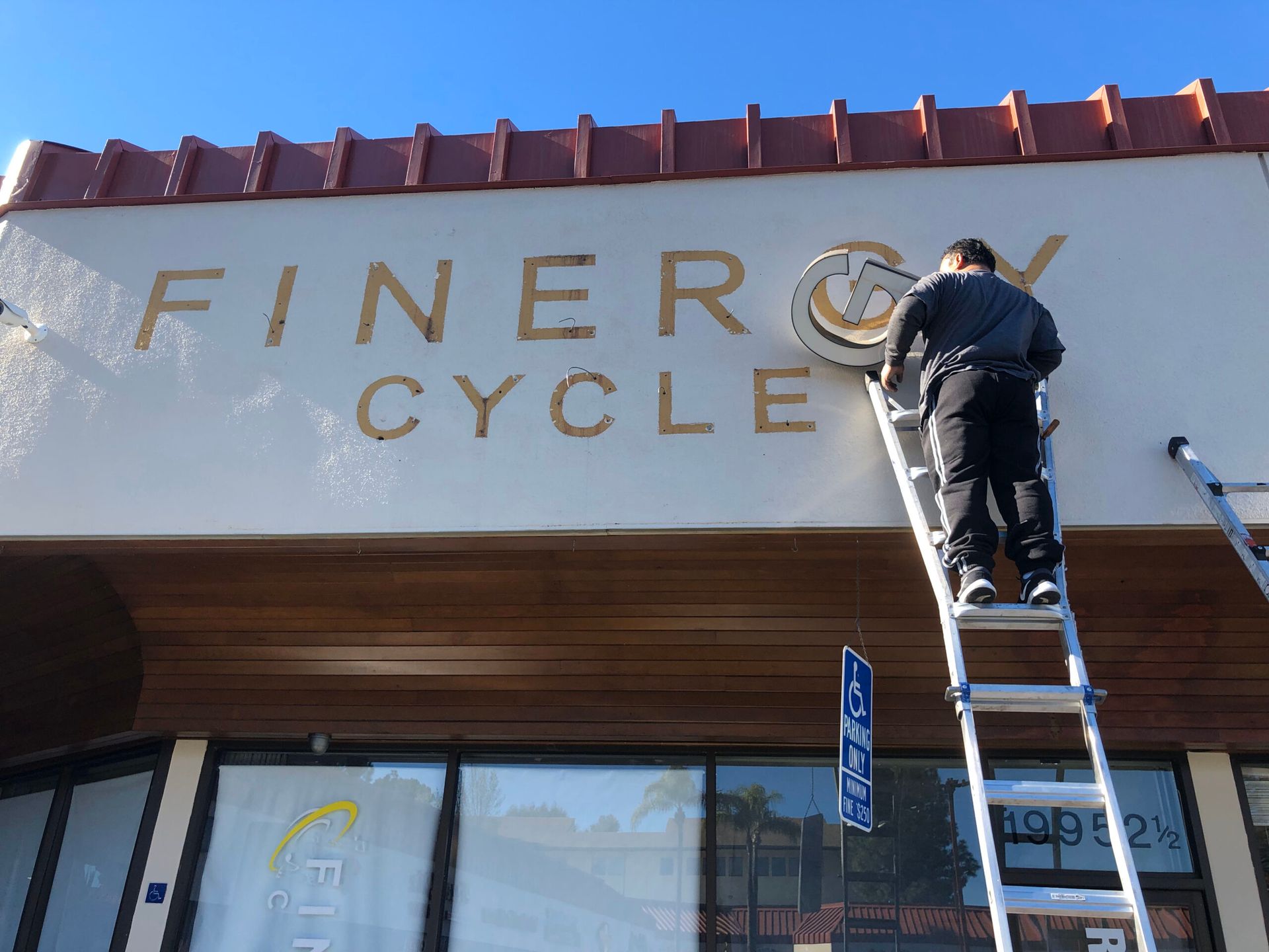 A man on a ladder is working on a sign for finer cycle