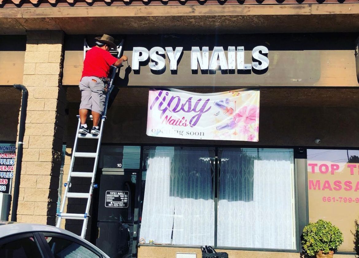 A man on a ladder painting a sign for psy nails