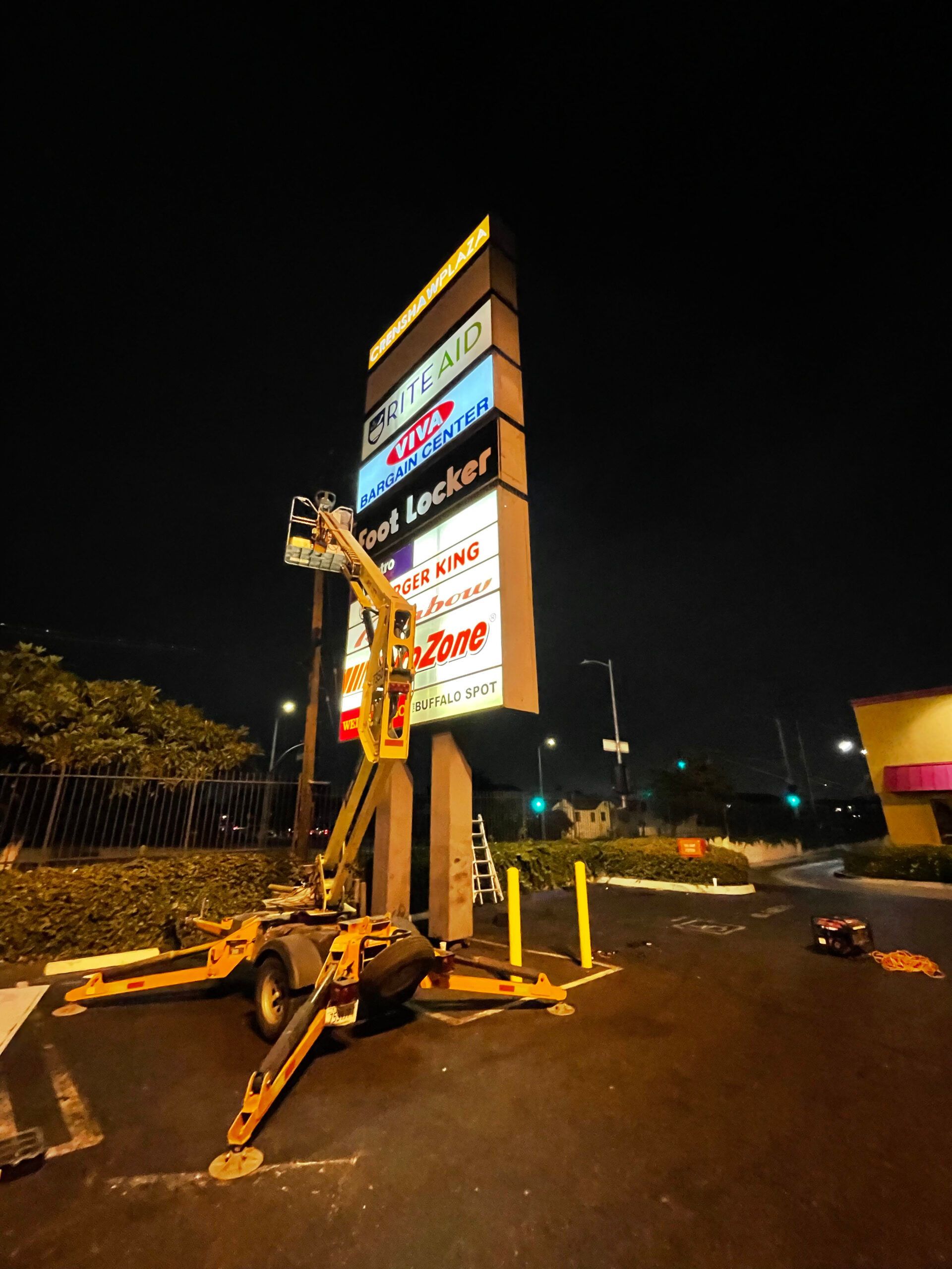 A large billboard is being installed at night in a parking lot.