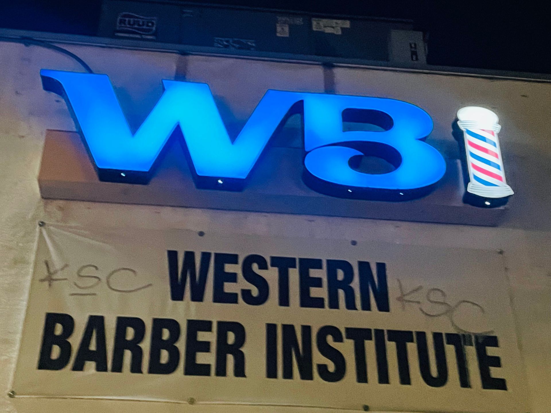 A sign for the western barber institute is lit up at night
