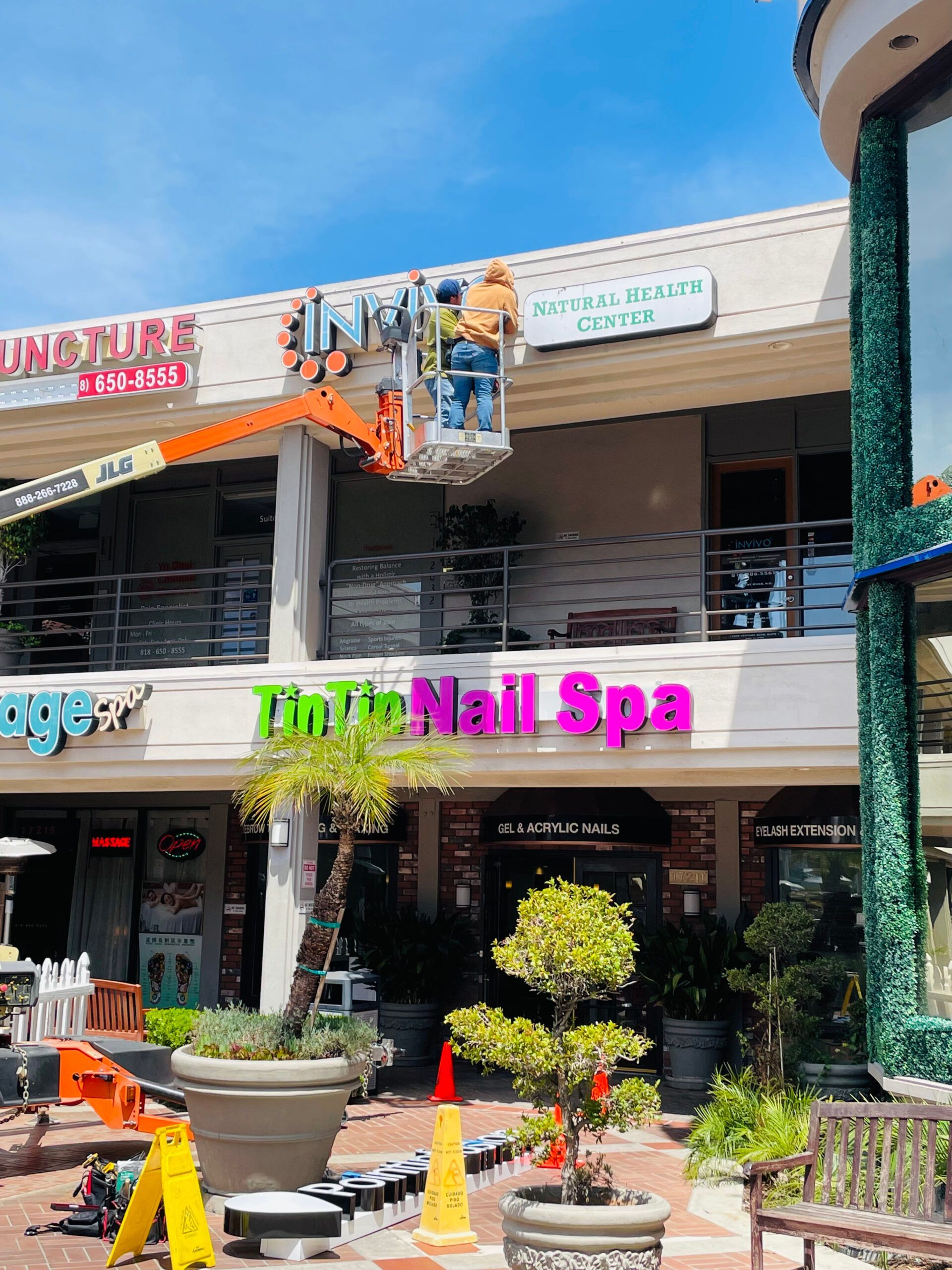 A man in a crane is hanging a sign for a nail spa