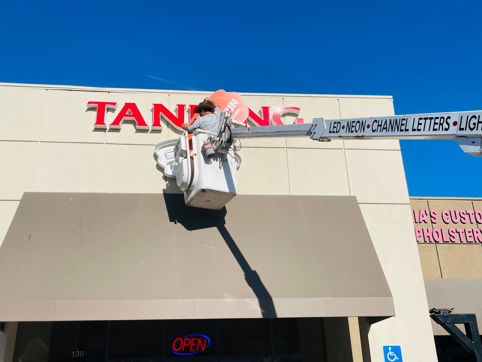 A man in a bucket is painting the tanning sign on a building