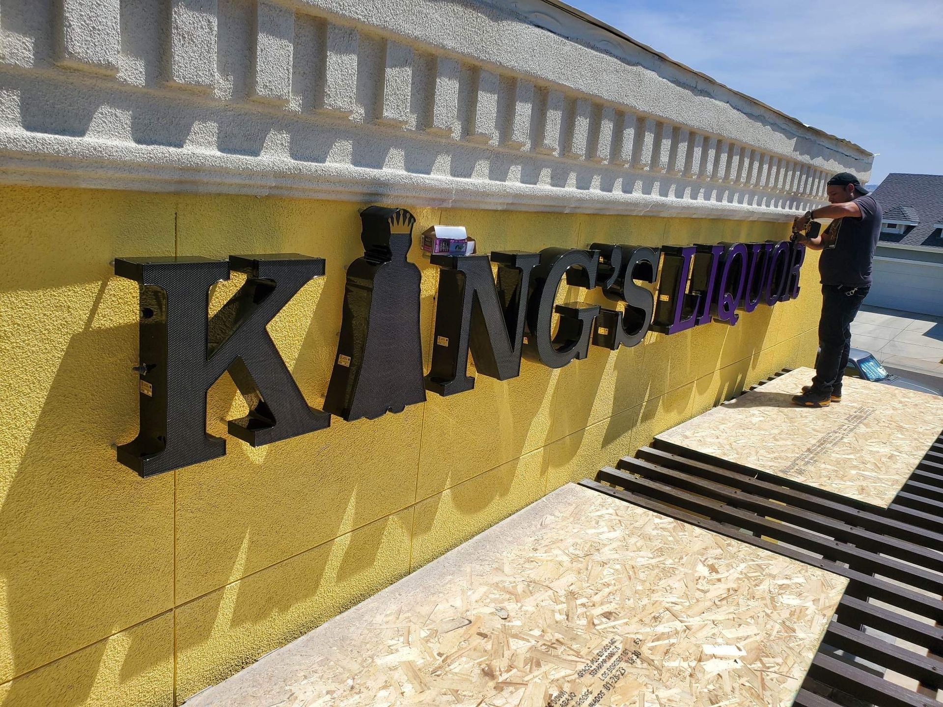A man is working on a sign that says kings liquor