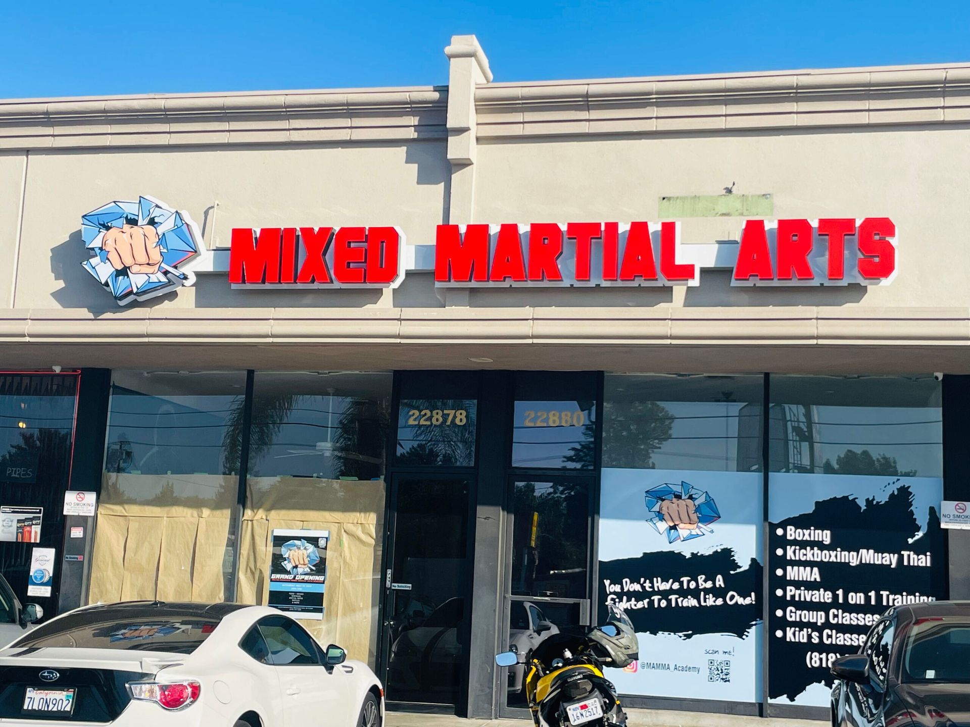 A white car is parked in front of a building that says mixed martial arts.