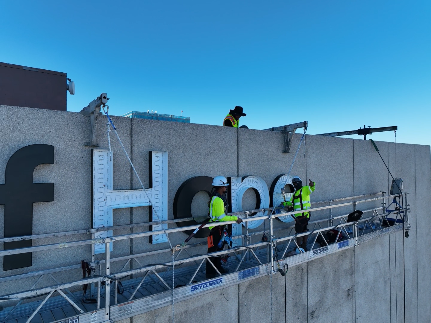 A group of men are working on a sign on top of a building.