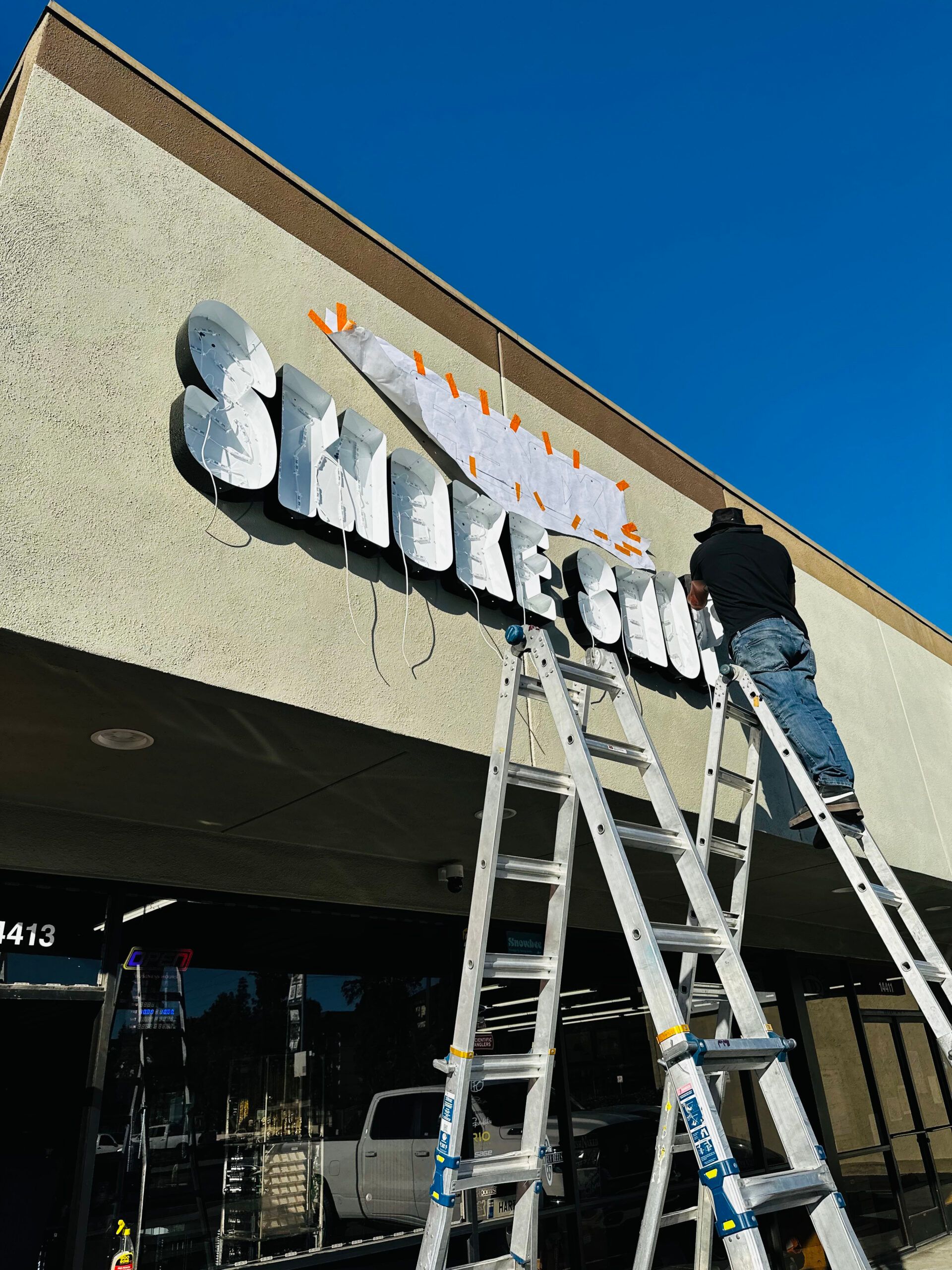A man on a ladder is installing a sign for smoke city