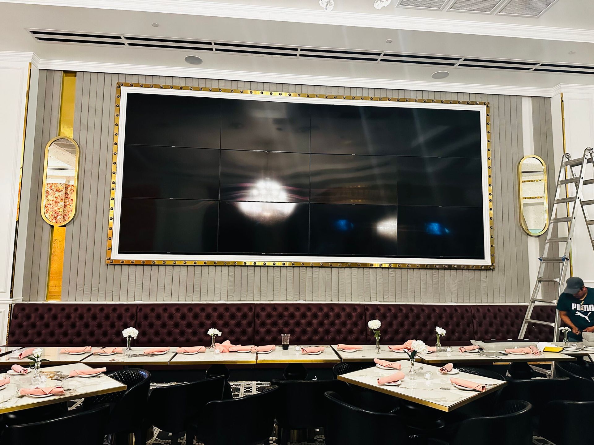 A restaurant with tables and chairs and a large screen on the wall.