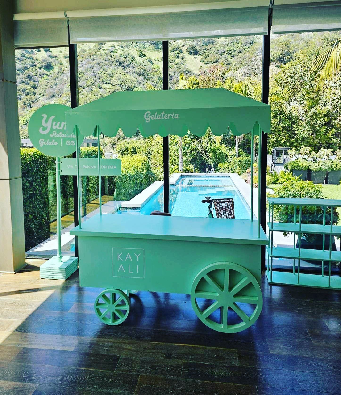 A green cart is sitting in front of a large window.
