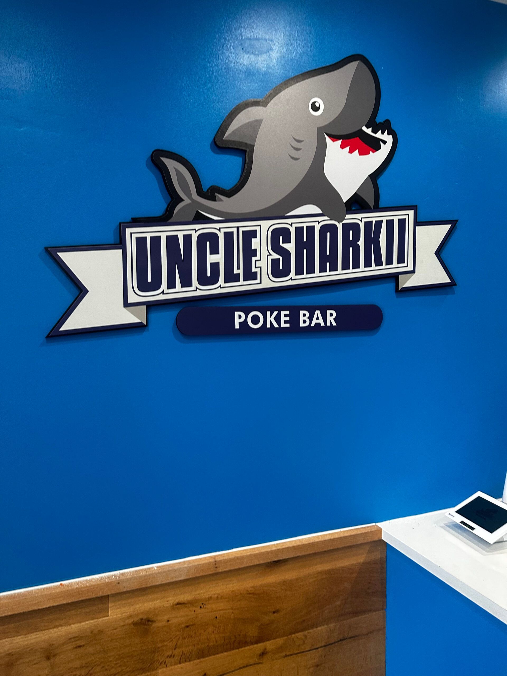 A sign for uncle sharkii poke bar on a blue wall