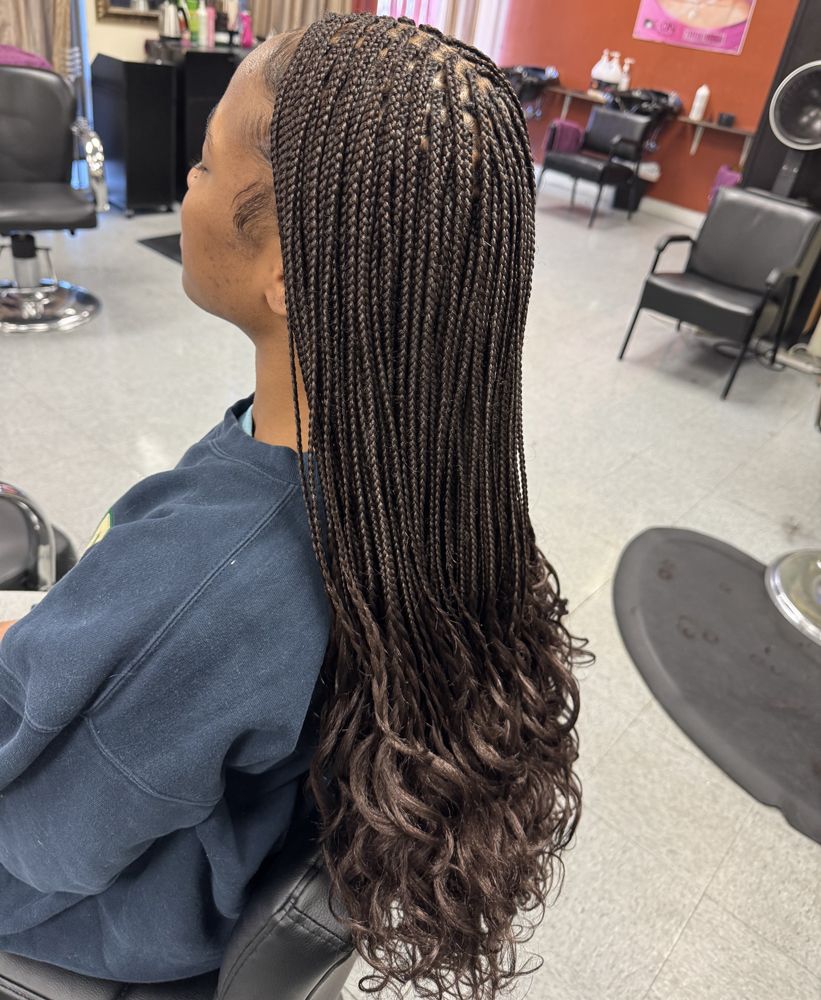 Person with micro braids, brown hair, sitting in a salon chair, with wavy ends.