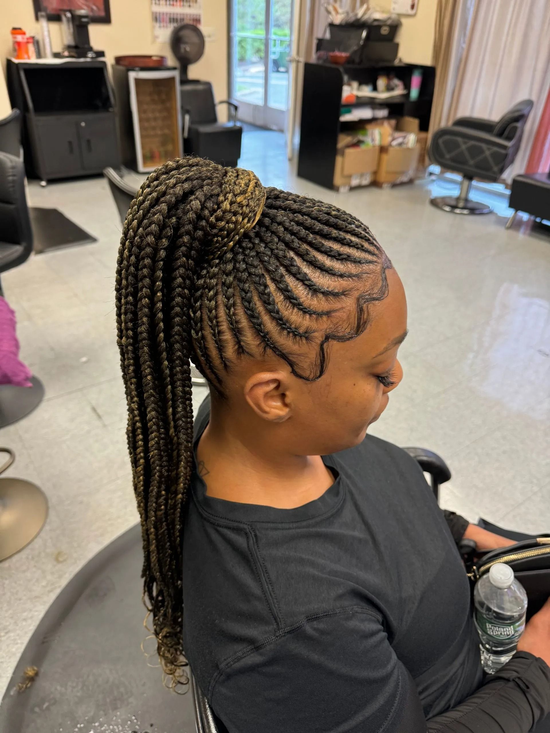 Woman with braided hair in a high ponytail, side profile. Braids are black and brown. Sitting in salon chair.