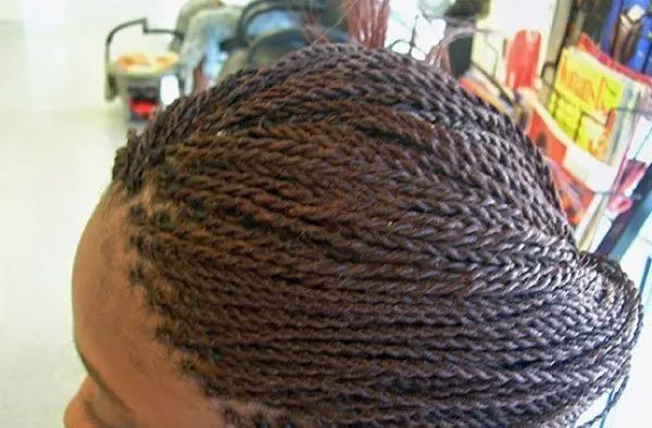 Close-up of a person's head with neatly styled brown micro twists, possibly in a salon setting.