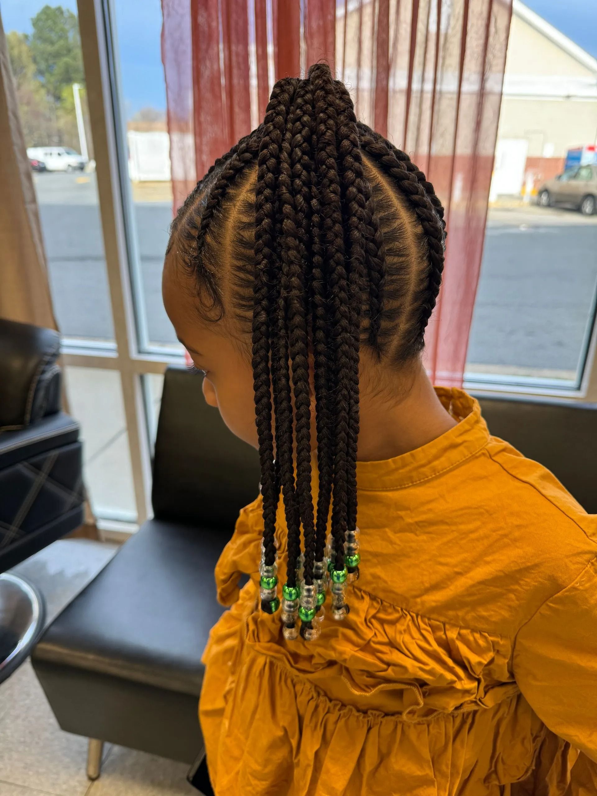 Young girl with braided hairstyle, wearing a yellow shirt, near a window.