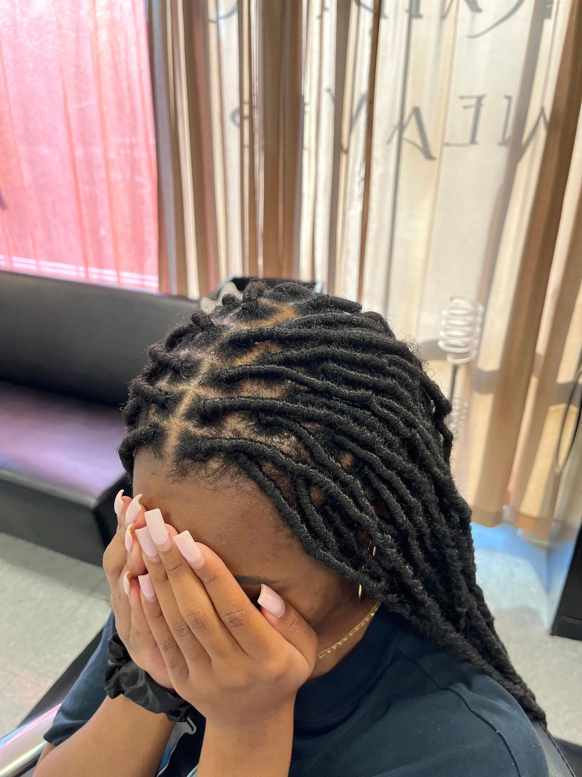 Person with dark hair in locs covers face with hands; light pink nails.