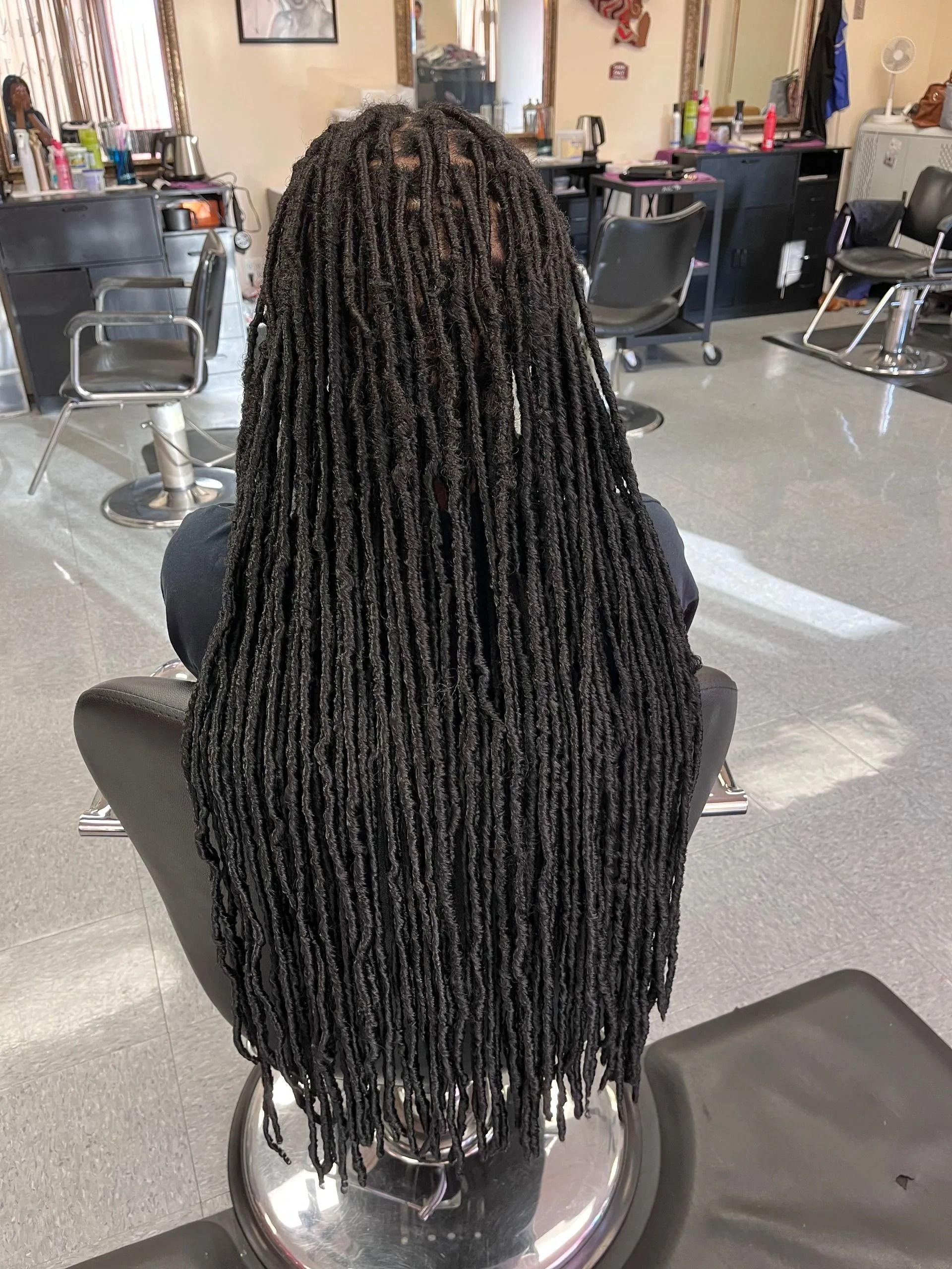 Woman with long black micro locs in a salon chair.