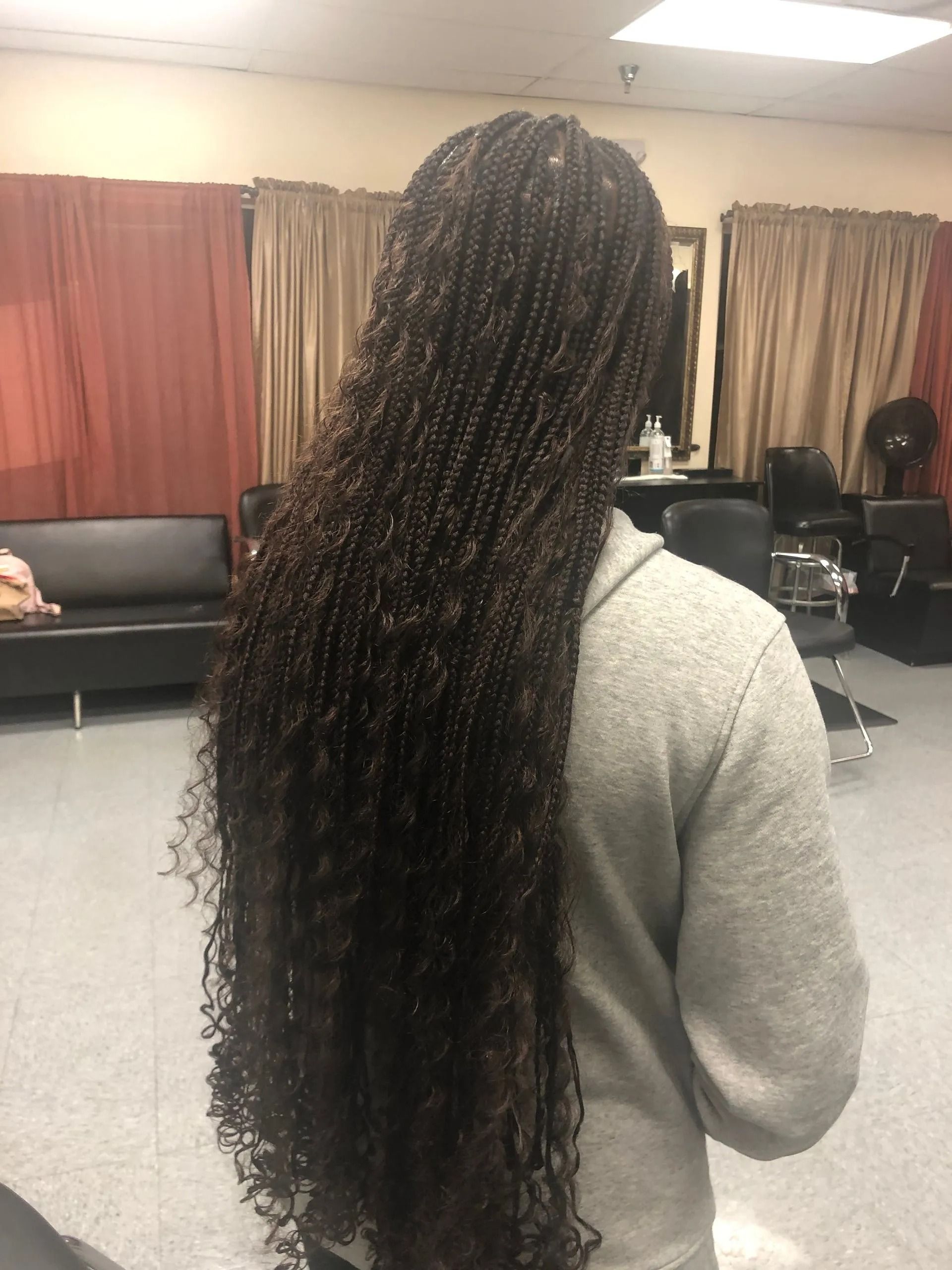 Person with long, dark curly braided hair stands in a salon.