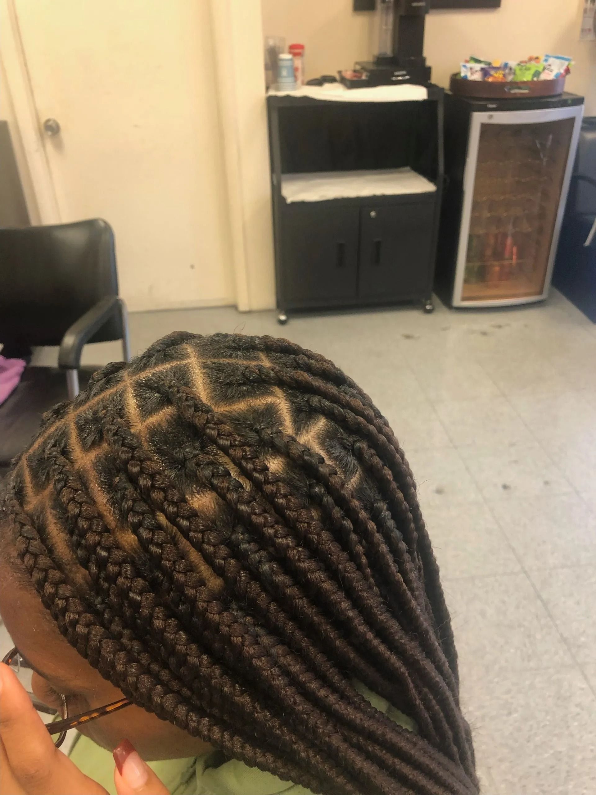 Person with dark hair in box braids, some with a zig-zag pattern at the top. Indoors, at a salon.