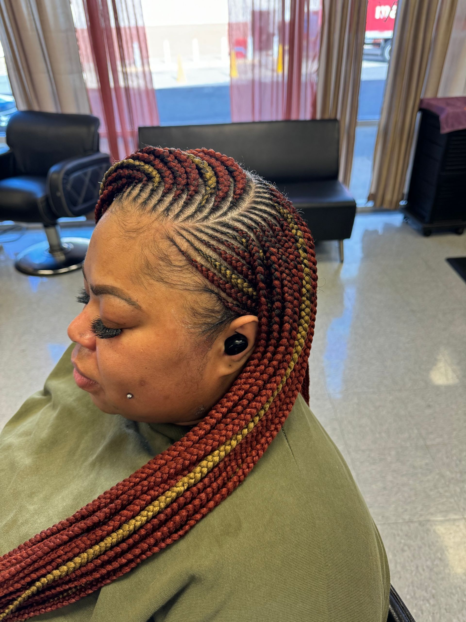 Woman with burgundy and gold braided hairstyle, seated in a salon.