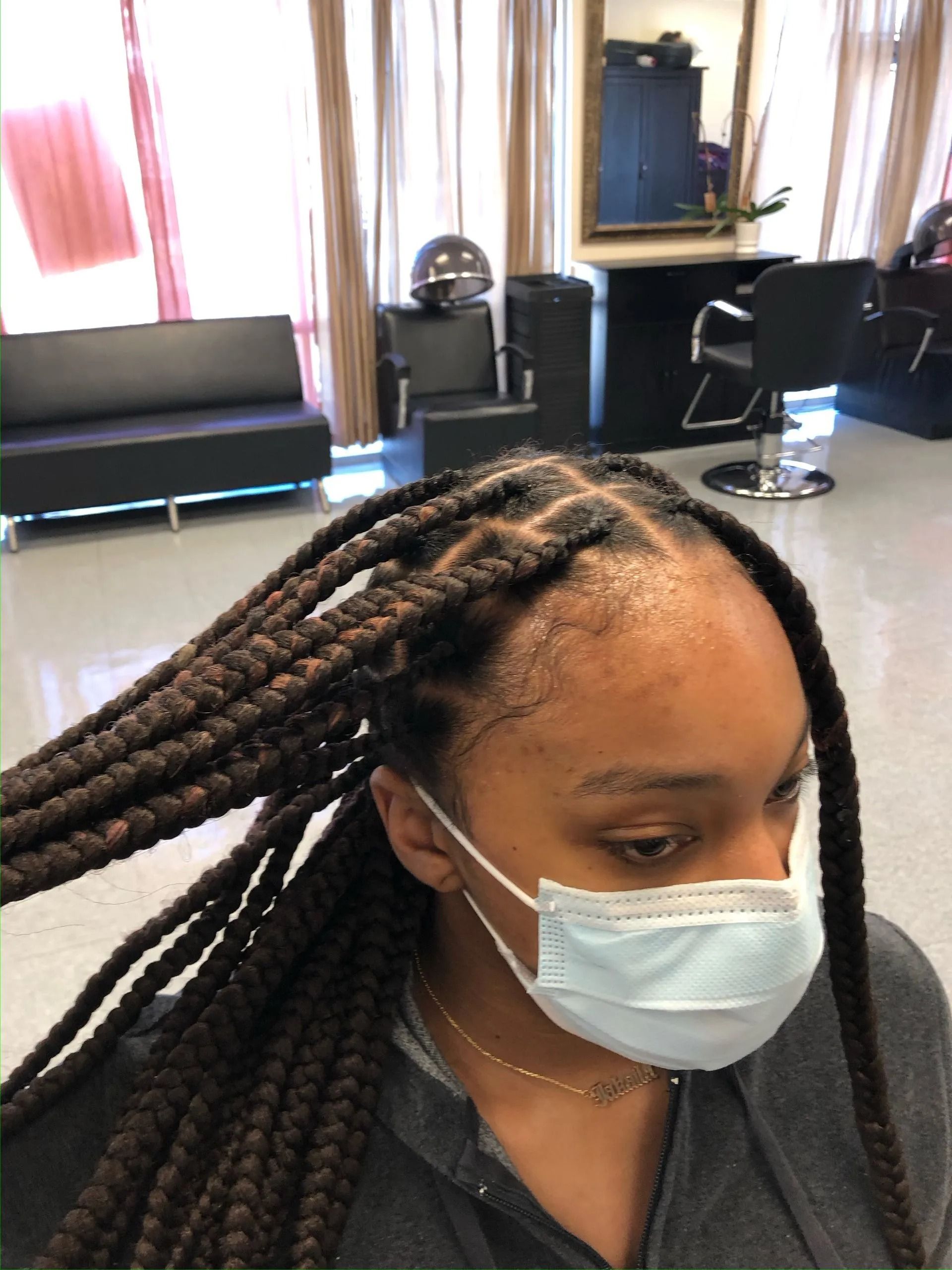 Person with braided hair wearing a mask in a salon.