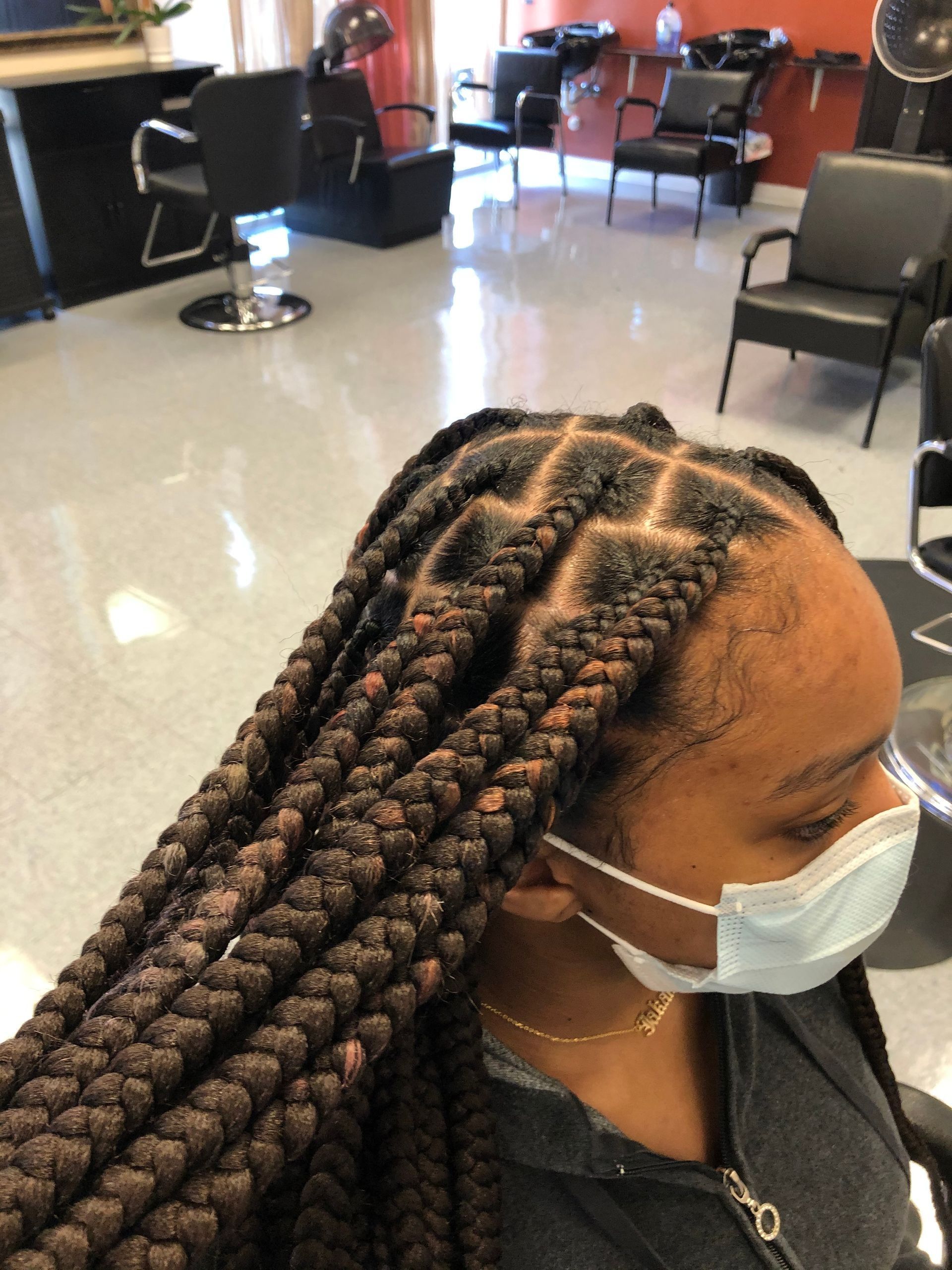Black woman with box braids, wearing a mask, in a hair salon.