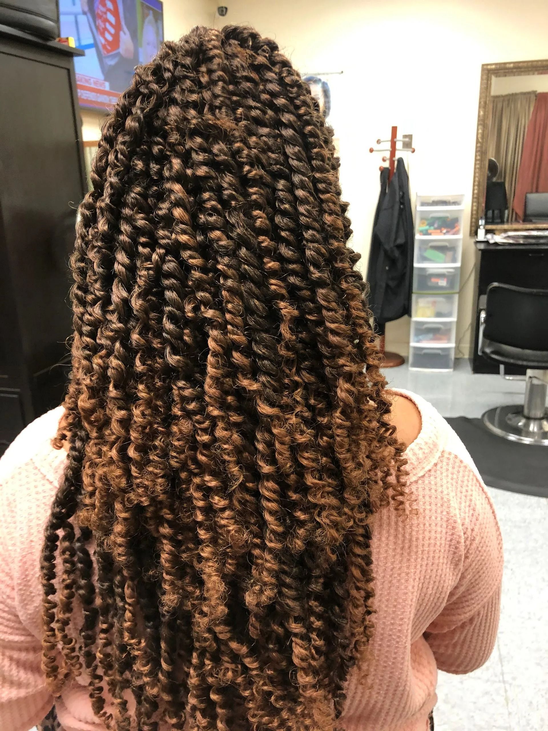 Woman with long, brown passion twists. The hair is styled down the back, in a salon setting.