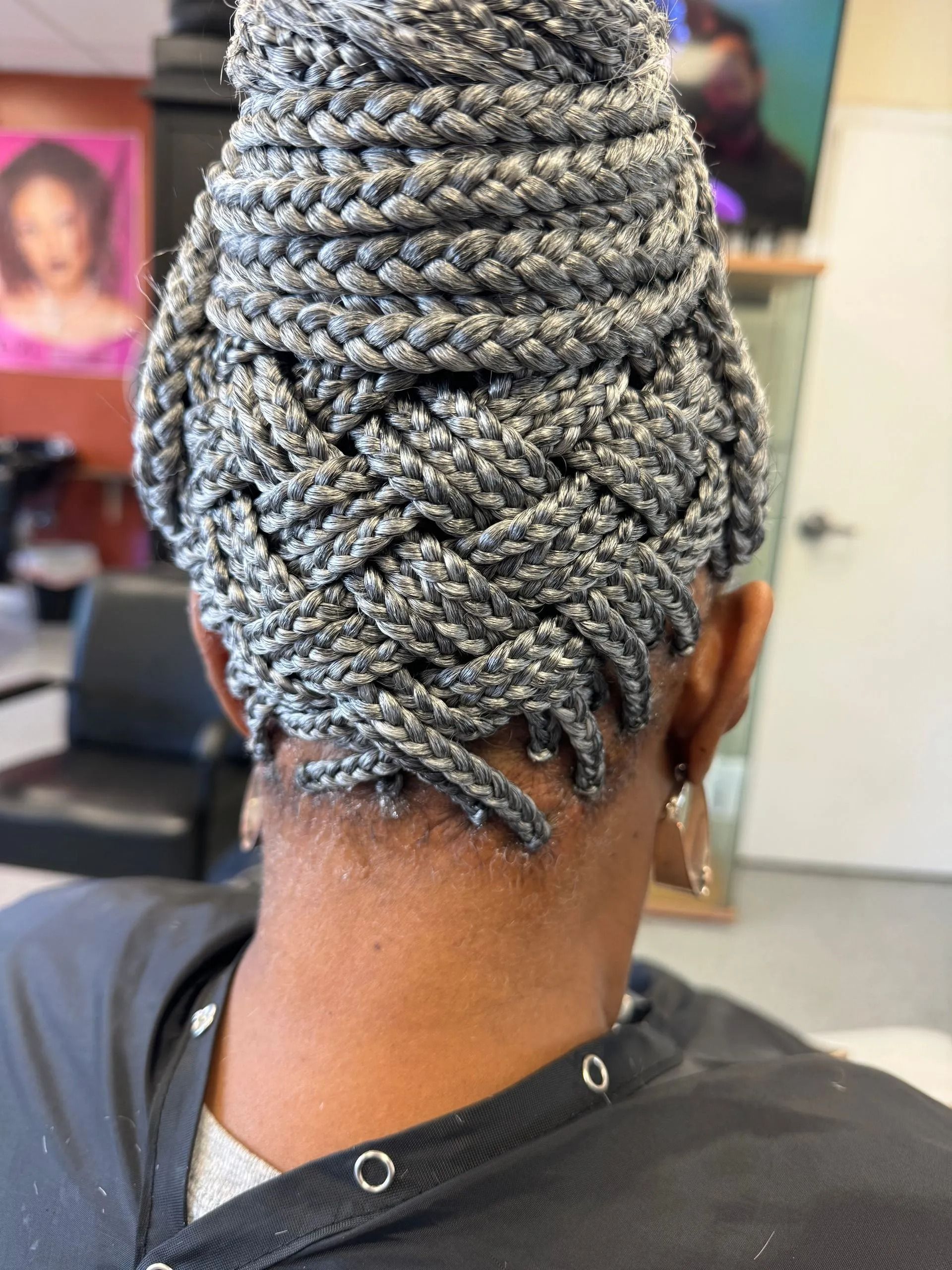 Back view of a Black woman with grey box braids styled in a bun with a zigzag pattern at the nape.