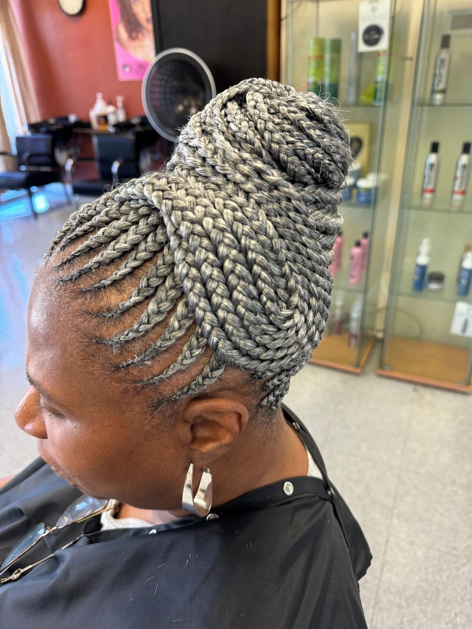 Woman with gray braided hair in a bun, wearing a salon cape.
