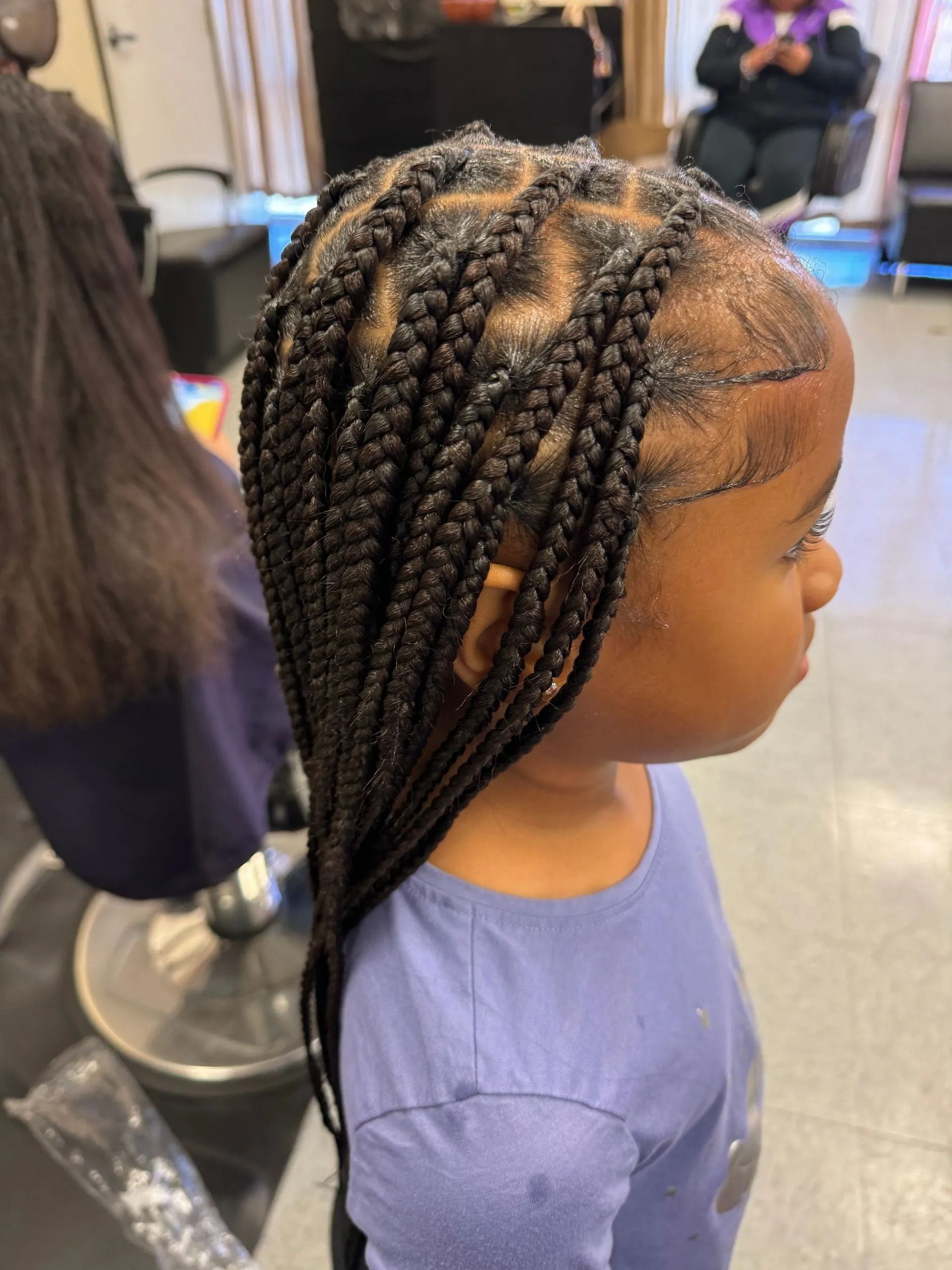 Young girl with braided hair at a salon, wearing a blue shirt.