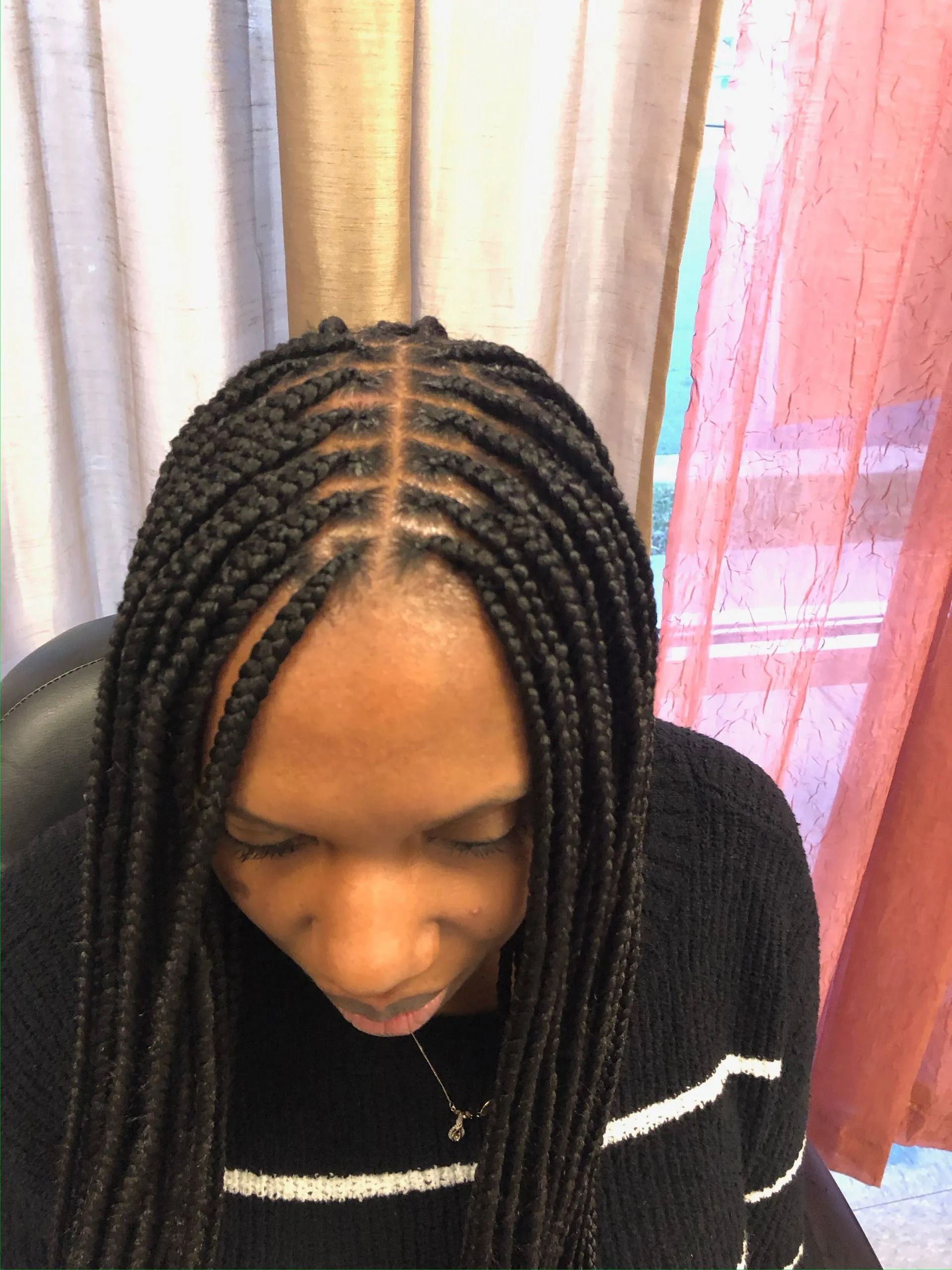 Woman with box braids, looking down. Black hair, dark skin, black sweater, neutral background.