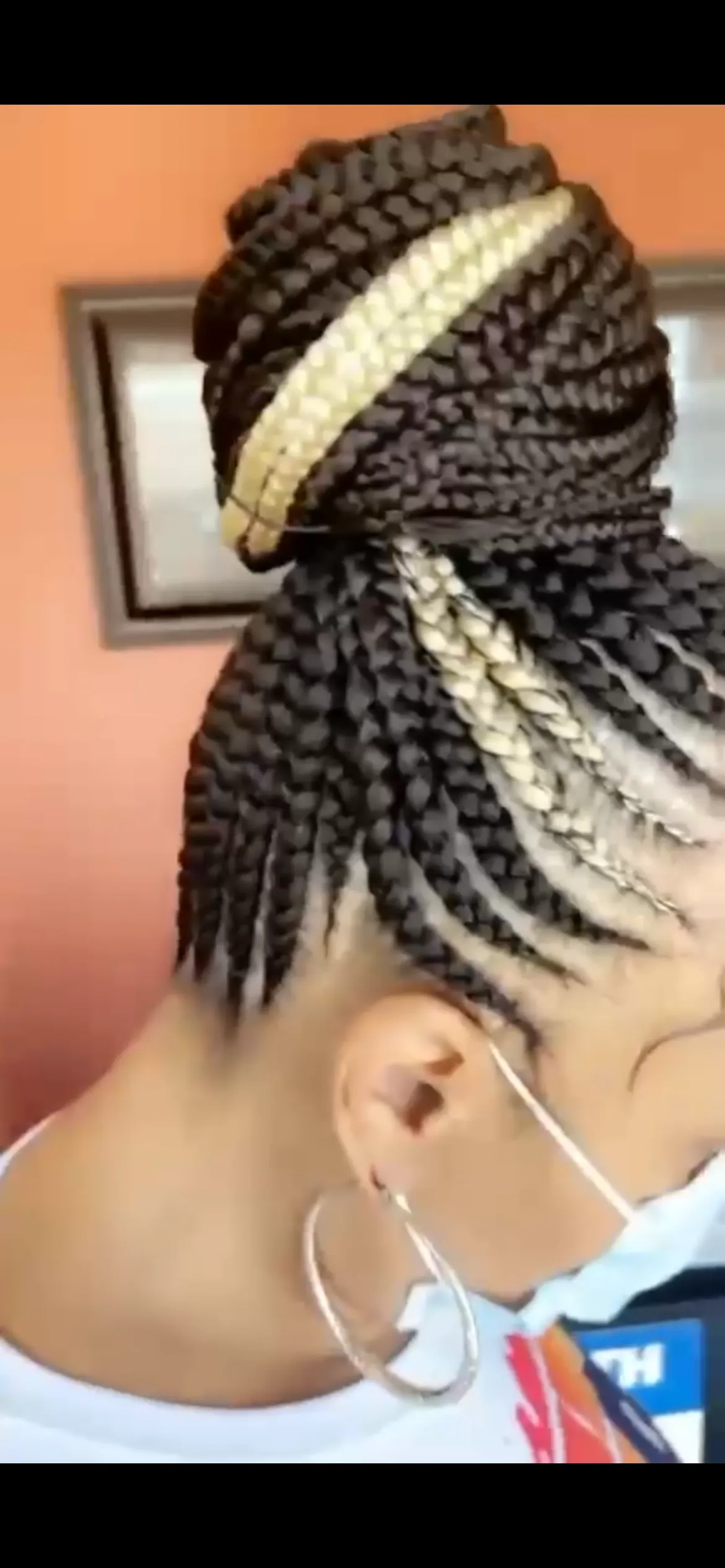 Woman with braided hairstyle, wearing a mask and hoop earrings.